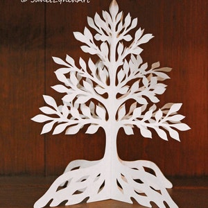 May include: White paper cut-out of a tree with intricate branches and leaves. The tree has a thick trunk and roots that spread out at the base.