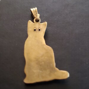 May include: Gold-toned metal pendant shaped like a sitting cat. The pendant has a loop at the top for attaching to a chain.