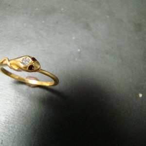 May include: A gold snake ring with a single clear stone and two red stones on the snake's head.