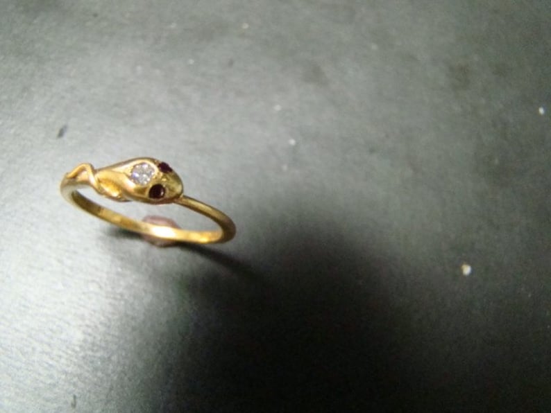 May include: A gold snake ring with a single clear stone and two red stones on the snake's head.