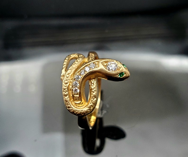 May include: A gold snake ring with emerald eyes and a row of diamonds around the body.