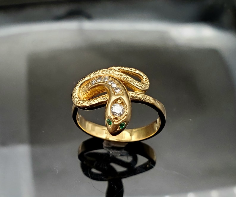 May include: A gold snake ring with a diamond and green stones for eyes.