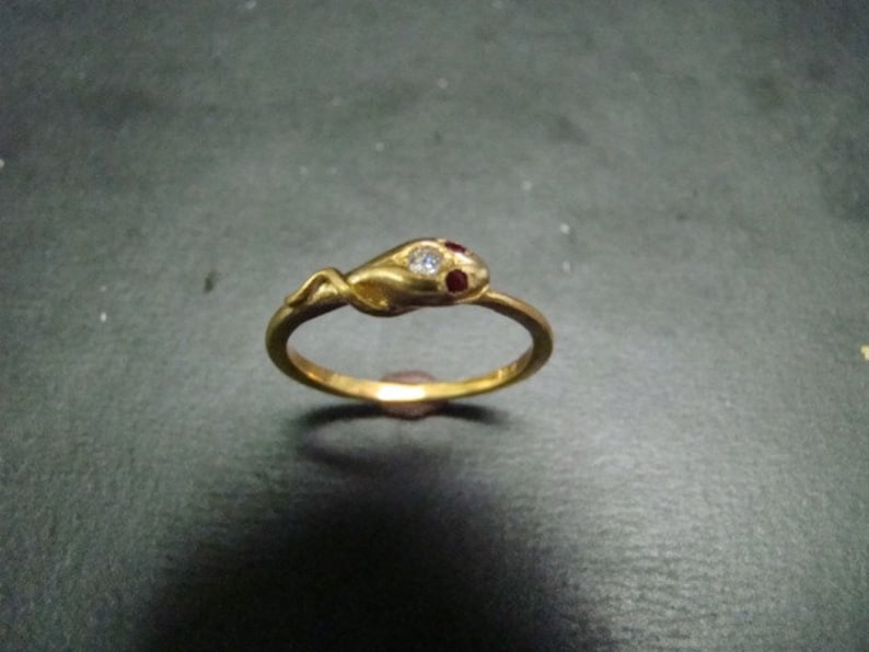 May include: A gold snake ring with red and white gemstones. The snake is coiled and has a detailed design.