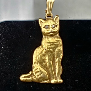 May include: A gold-toned cat pendant with diamond eyes. The cat is sitting with its tail curled around its legs.