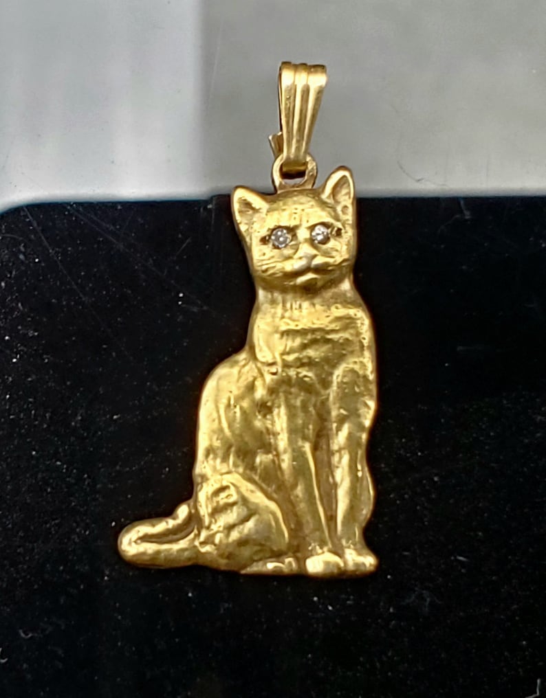 May include: A gold-toned cat pendant with diamond eyes. The cat is sitting with its tail curled around its legs.