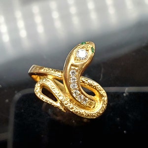 May include: A gold snake ring with a diamond and green stones on the head.