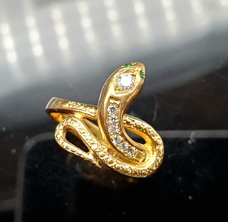 May include: A gold snake ring with a diamond and green stones on the head.