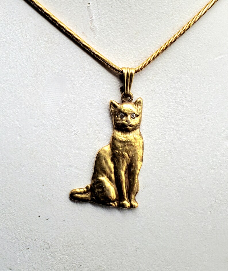 May include: A gold chain necklace with a gold cat pendant. The cat has diamond eyes.