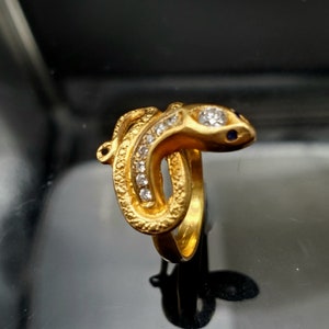 May include: A gold snake ring with clear stones and blue accents.