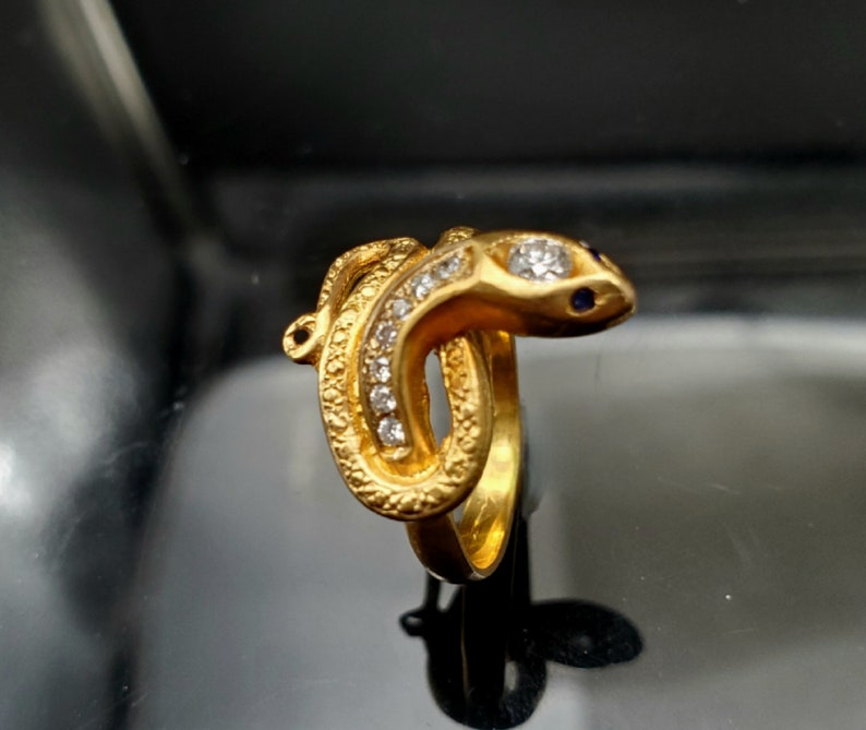 May include: A gold snake ring with clear stones and blue accents.