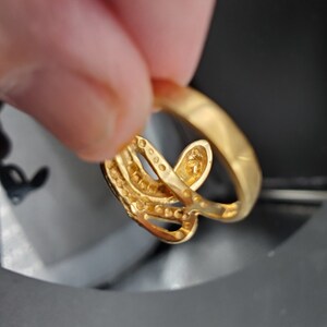 May include: A gold ring with a delicate, intricate design featuring multiple intertwined bands. The ring is adorned with small, sparkling stones.