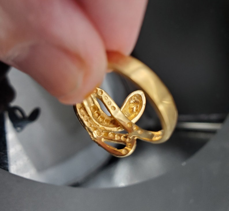 May include: A gold ring with a delicate, intricate design featuring multiple intertwined bands. The ring is adorned with small, sparkling stones.