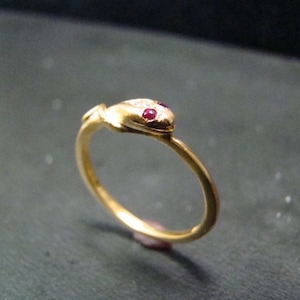 May include: A gold snake ring with red ruby eyes. The ring is made of gold and has a simple design.