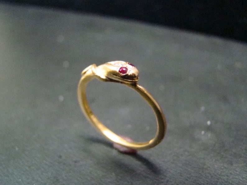 May include: A gold snake ring with red ruby eyes. The ring is made of gold and has a simple design.