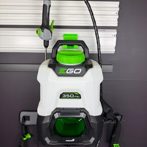 May include: A white and black EGO 350 PSI battery-powered backpack sprayer with green accents. The sprayer has a black hose and a gray and green nozzle. The sprayer is mounted on a wall with a black bracket.