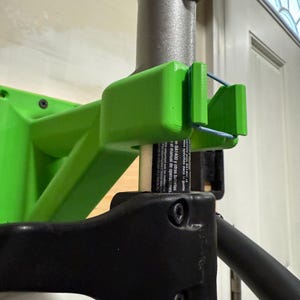 May include: A green and black wall mount for a pole saw. The mount has a black plastic handle and two screws. The pole saw is not included.