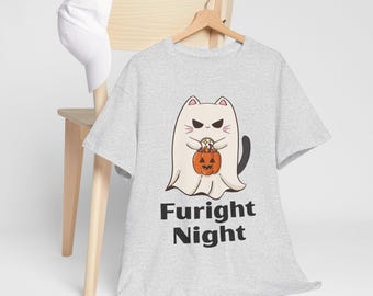 May include: A light gray t-shirt with a Halloween-themed graphic. The graphic features a cartoon cat dressed as a ghost, holding a pumpkin. The text "Fright Night" is printed below the graphic. A white baseball cap rests on a wooden chair.