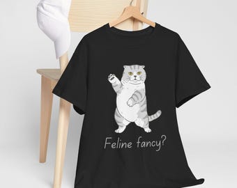 May include: Black t-shirt with a white and gray cartoon cat wearing a surprised expression. The cat is standing on its hind legs with its front paws raised. The text "Feline fancy?" is printed below the cat.
