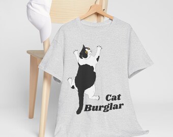Może przedstawiać: Szary T-shirt z ilustracją czarno-białego kota i nadrukiem "Cat Burglar" z przodu.
