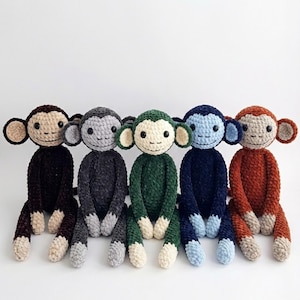 May include: Five handmade crochet monkey dolls in various colors: black, gray, green, blue, and orange. Each monkey has a light beige face, ears, and feet, with black button eyes and a stitched smile. The monkeys are sitting upright.