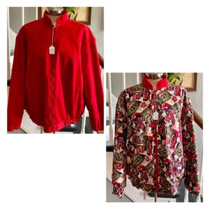 May include: Two jackets are displayed. The first is a solid red, zip-up jacket with a stand-up collar and elastic cuffs and hem. The second jacket has a colorful pattern with red, green, and blue elements. Both jackets have a tag attached to the zipper.