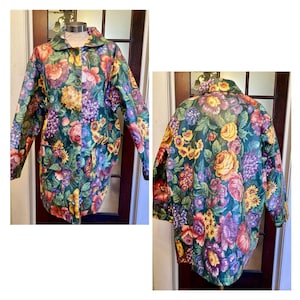 May include: A floral print coat with a dark green background and a variety of colorful flowers. The coat has a button-up front, a collar, and long sleeves. The coat is displayed on a mannequin.