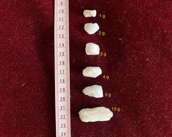 May include: Six white rock crystals of varying sizes on a red velvet surface. The crystals are labeled with their weight in grams: 1g, 2g, 3g, 4g, 5g, and 13g.