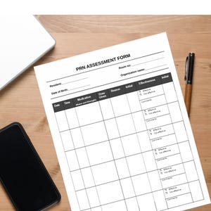 May include: A white PRN Assessment Form with black text, a pen, a smartphone, and a laptop on a wooden surface. The form includes fields for resident information, medication details, and effectiveness assessment.
