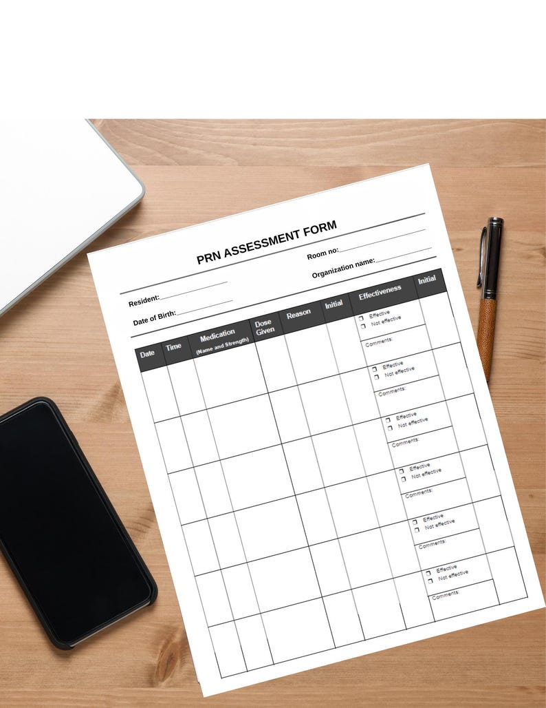 May include: A white PRN Assessment Form with black text, a pen, a smartphone, and a laptop on a wooden surface. The form includes fields for resident information, medication details, and effectiveness assessment.