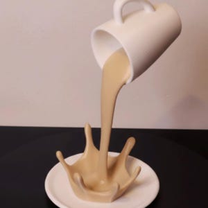 Puede incluir: Una taza de cerámica blanca inclinada, vertiendo un chorro de líquido beige en forma de salpicadura sobre un platillo blanco. La taza tiene un asa. La salpicadura es una representación artística detallada de un impacto líquido.