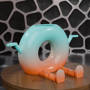 Puede incluir: Una tetera de cerámica caprichosa en forma de rosquilla, con un degradado de colores, que va del turquesa al naranja. Cuenta con dos picos y patas articuladas en tonos naranja a juego, apoyada sobre una superficie de madera. Un objeto decorativo único.