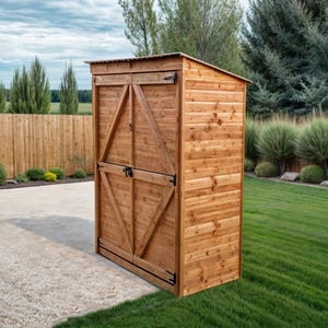 Puede incluir: Un cobertizo de almacenamiento de madera alto, con techo inclinado y puertas dobles. El cobertizo está construido con tablones de color marrón claro y tiene herrajes negros. Se encuentra sobre una superficie de hormigón, rodeado de césped verde y una valla de madera.