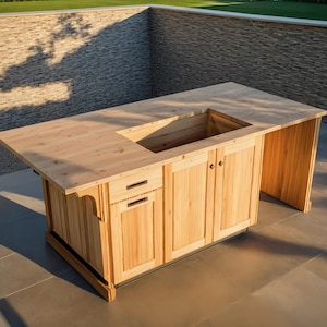 Op de afbeelding: Een lichtgekleurd houten buitenkeuken eiland met een rechthoekig aanrechtblad en een verzonken gedeelte. Het eiland heeft kastdeuren, een lade en een zijpaneel. De structuur is gemaakt van lichtgekleurd hout.