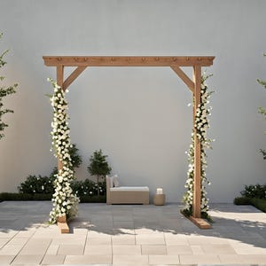 Puede incluir: Un arco de boda de madera adornado con flores blancas, sobre un fondo neutro. El arco está flanqueado por vegetación y árboles, creando un ambiente exterior sereno. Un pequeño banco y una vela completan el ambiente.