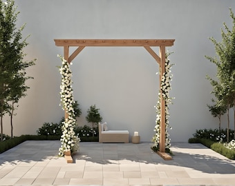 May include: A wooden wedding arch adorned with white flowers, set against a neutral backdrop. The arch is flanked by greenery and trees, creating a serene outdoor setting. A small bench and candle add to the ambiance.