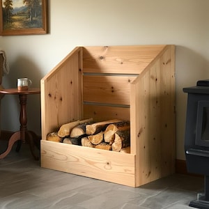 May include: A light-colored wooden firewood storage rack. The rack is rectangular with an angled top and horizontal supports. It is filled with cut logs. The rack is next to a black stove.