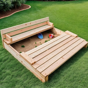 Puede incluir: Un arenero de madera con un banco incorporado y una tapa con bisagras. El arenero está lleno de arena y tiene una pala azul y una taza roja dentro. El arenero está sobre un césped verde.