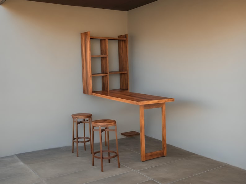 Puede incluir: Un escritorio de pared de madera con una estanter&iacute;a empotrada y dos taburetes a juego. El escritorio tiene una encimera rectangular y una sola pata. Los taburetes son redondos con un dise&ntilde;o sencillo. Los muebles son de madera marr&oacute;n claro.