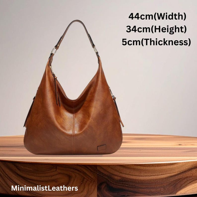 May include: A brown leather shoulder bag with a curved design. The bag is 17 inches wide, 13 inches high, and 2 inches thick. It has a single strap and a minimalist design. The text "MinimalistLeathers" is at the bottom.