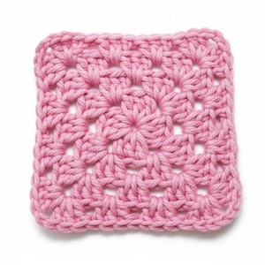 May include: A square, hand-crocheted item in a soft pink hue. The stitch pattern creates a textured, open design with a central floral motif. The edges are neatly finished, showcasing the craftsmanship of the piece. This item could be a washcloth or part of a larger project.