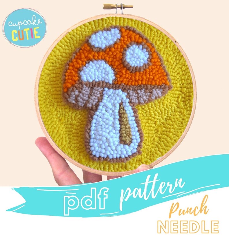 May include: A punch needle pattern for a mushroom with a brown stem, orange and white cap, and white spots. The pattern is on a yellow background and is in a wooden embroidery hoop.