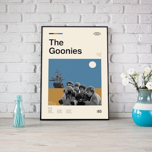 May include: A black framed poster with a minimalist design featuring a blue and yellow colour scheme. The poster has the text "The Goonies" in bold black letters and a silhouette of a ship with a group of children in front of it. The poster also includes the year "1985" in the bottom right corner.