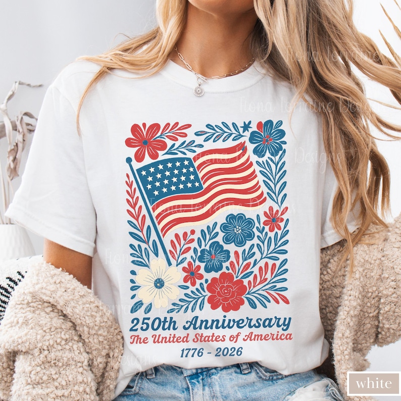 Puede incluir: Camiseta blanca con un dise&ntilde;o patri&oacute;tico. El gr&aacute;fico incluye una bandera estadounidense, rodeada de elementos florales rojos, azules y crema. El texto dice "250th Anniversary The United States of America 1776-2026."