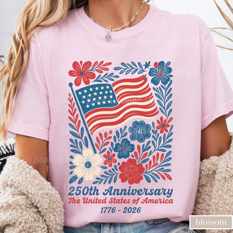 Puede incluir: Camiseta rosa claro con un dise&ntilde;o patri&oacute;tico. El gr&aacute;fico incluye una bandera estadounidense ondeando, rodeada de elementos florales rojos, blancos y azules. El texto dice "250th Anniversary The United States of America 1776-2026."