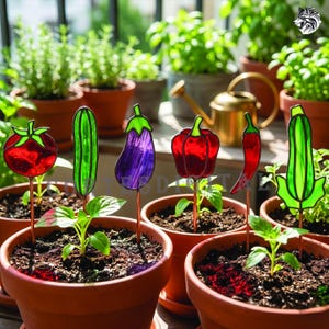 Puede incluir: Marcadores de jardín con forma de verduras, estilo vidriera. Representan un tomate, pepino, berenjena, pimiento, chile y calabacín. Cada marcador está montado sobre una estaca de cobre en una maceta de terracota.