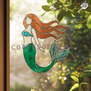 May include: A stained glass suncatcher shaped like a mermaid with long flowing orange hair, a teal top, and a green tail. The piece is outlined in dark metal solder and features a silver chain for hanging. The text CORTESDIGITAL is visible.