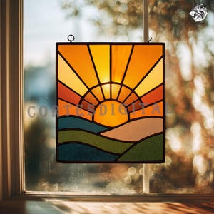 May include: Stained glass panel showing a sunset over rolling hills. The design features a vibrant orange and yellow sun with radiating rays, set against a backdrop of colourful landscape elements. The panel is framed in black and hangs from a small metal loop.