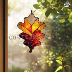 May include: Stained glass oak leaf in autumn colors. The leaf features shades of yellow, orange, and red, with a textured, light brown top section. The word "CORTES DIGITAL" is printed across the leaf. The leaf is hanging in front of a blurred background of green foliage.