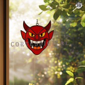 Puede incluir: Un vitral rojo con forma de cara de diablo con ojos amarillos, dientes negros y boca naranja. El diablo tiene cuernos y cuelga de una cadena. El texto "CORTES DIGITAL" es visible.