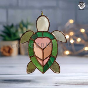May include: Stained glass turtle ornament with green, pink, and white sections. The turtle has a heart-shaped design in the center and is outlined with copper-colored metal. A small loop is at the top for hanging. The ornament is a decorative item.